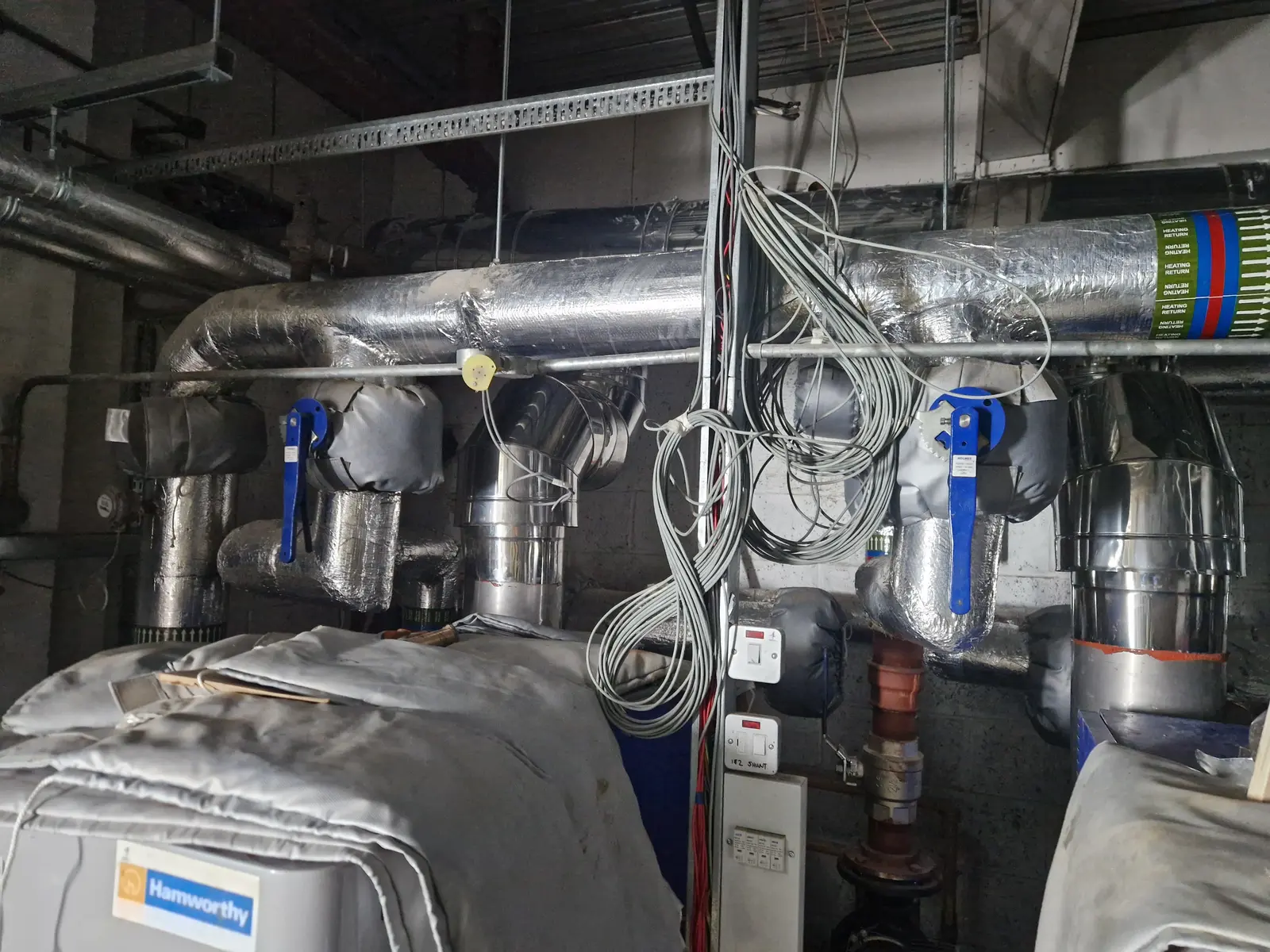 Existing stainless flue header and drop in a congested boiler plantroom, photographed on a survey