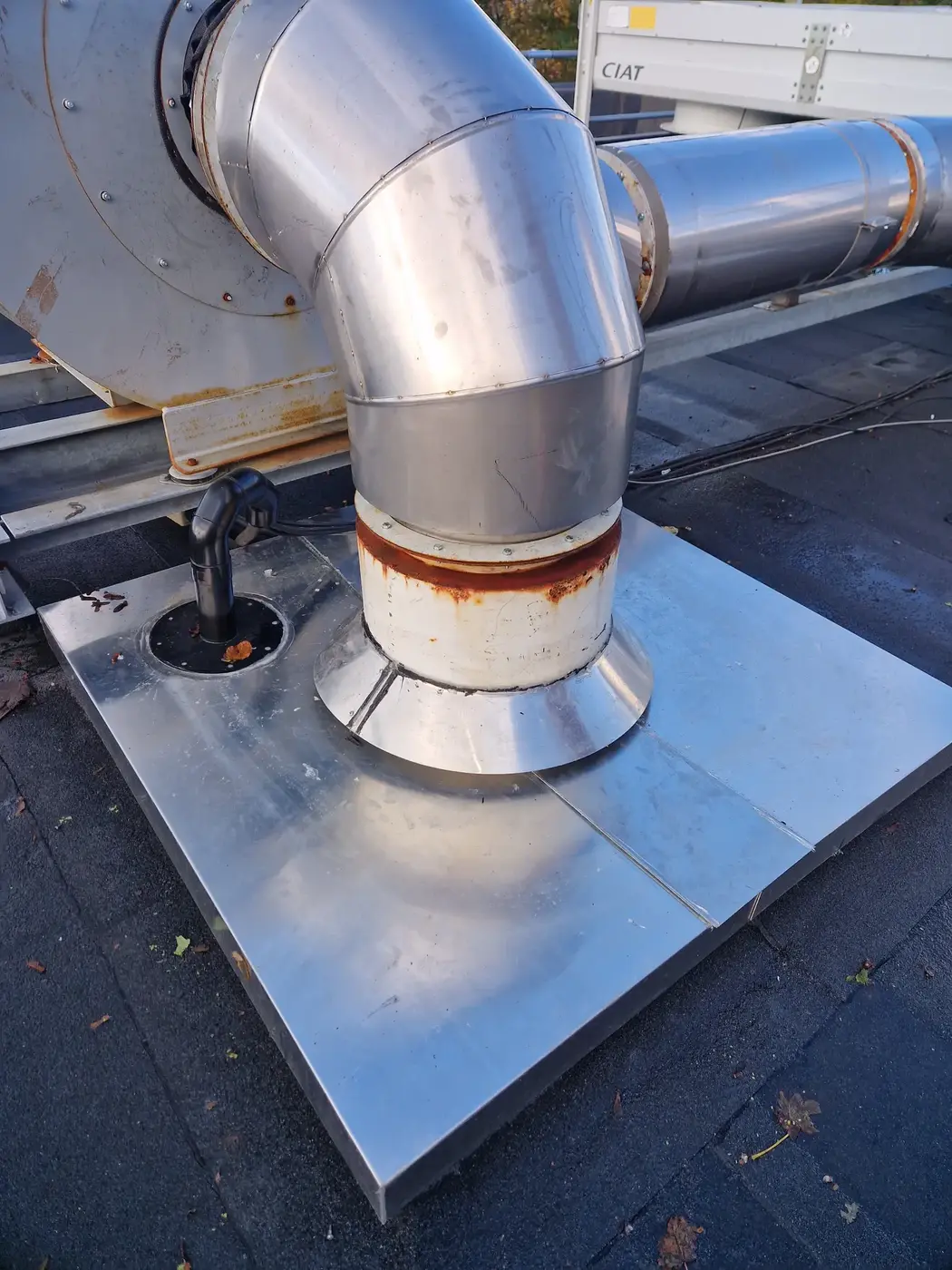 Stainless flue elbow at a wall plate with rust spots on the casing and cracked sealant around the penetration