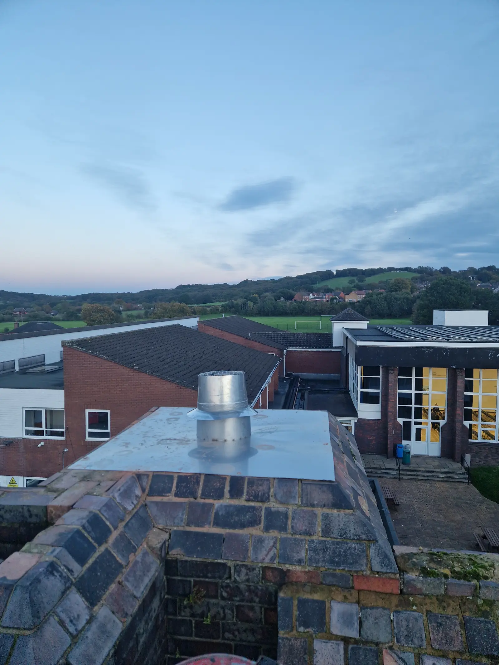 Stainless liner terminal and cap plate on top of an old brick school chimney at dusk