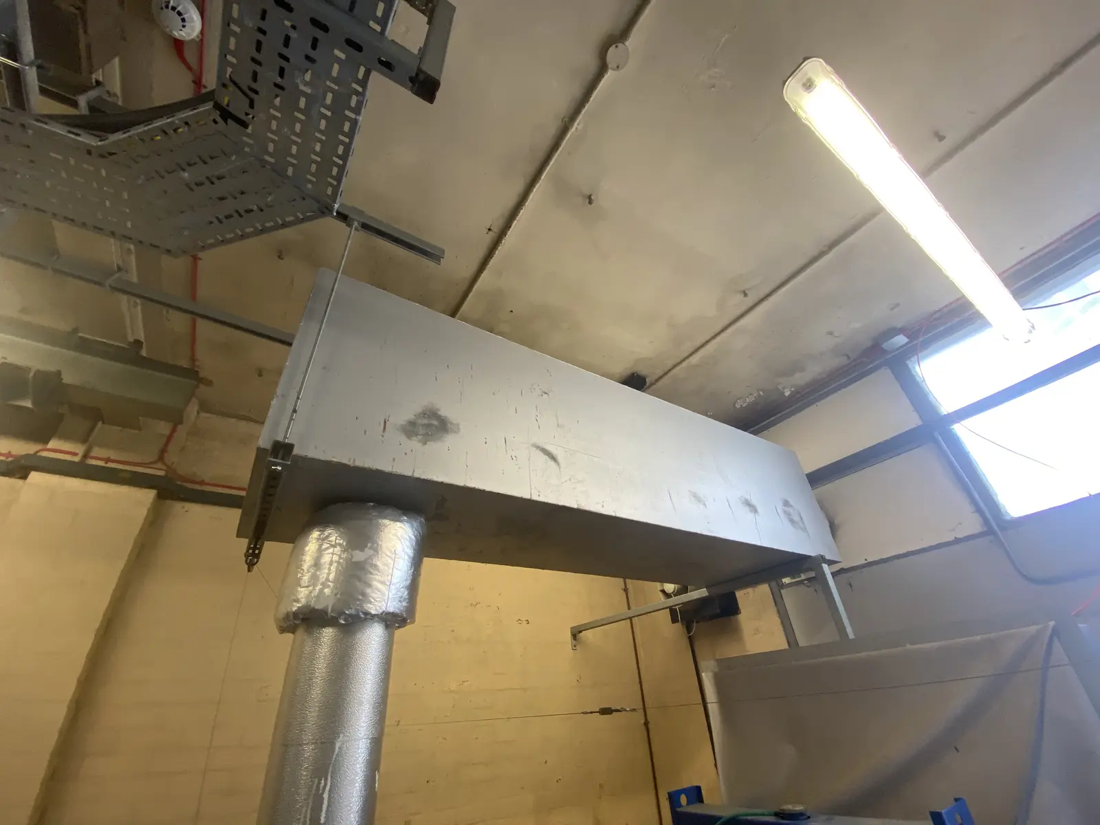 A horizontal flue run hung from a concrete soffit, where it comes out of a blockwork wall