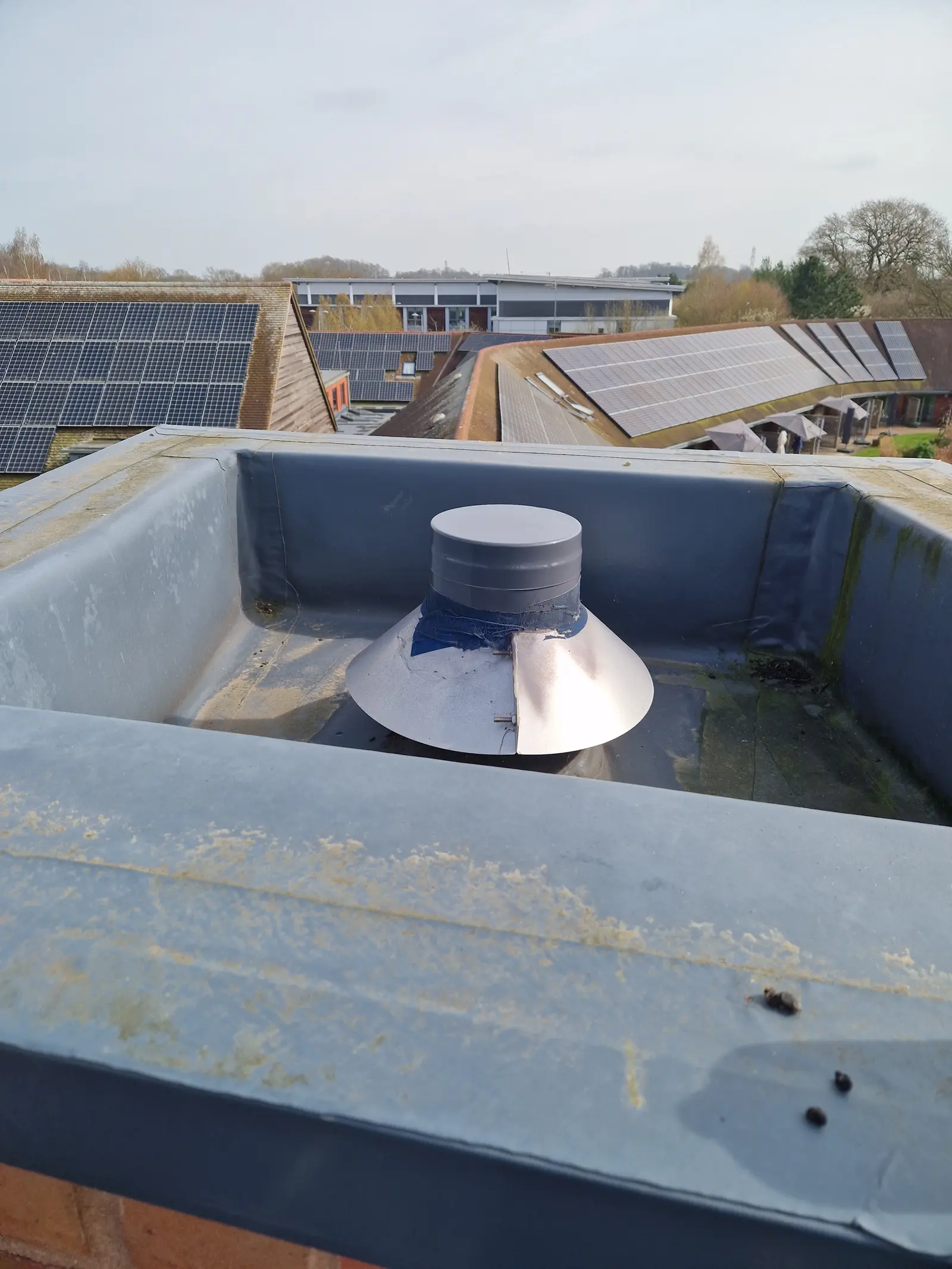 Stainless flue terminal sitting low behind a roof parapet with staining on the render