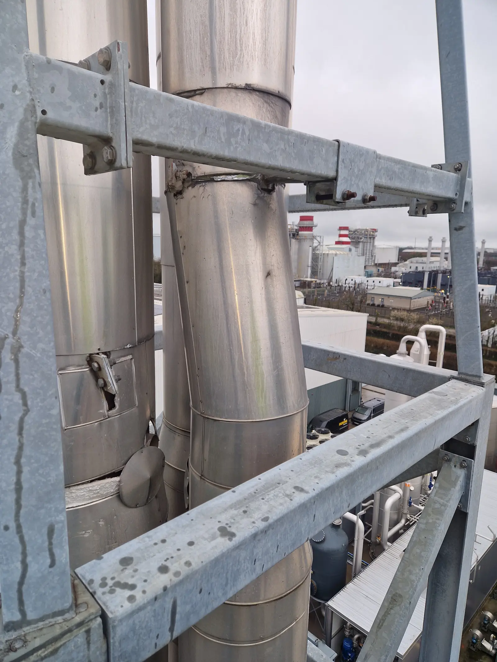 Flue support bracket strap pulled out of line around a mast, with worn paint at the fixings