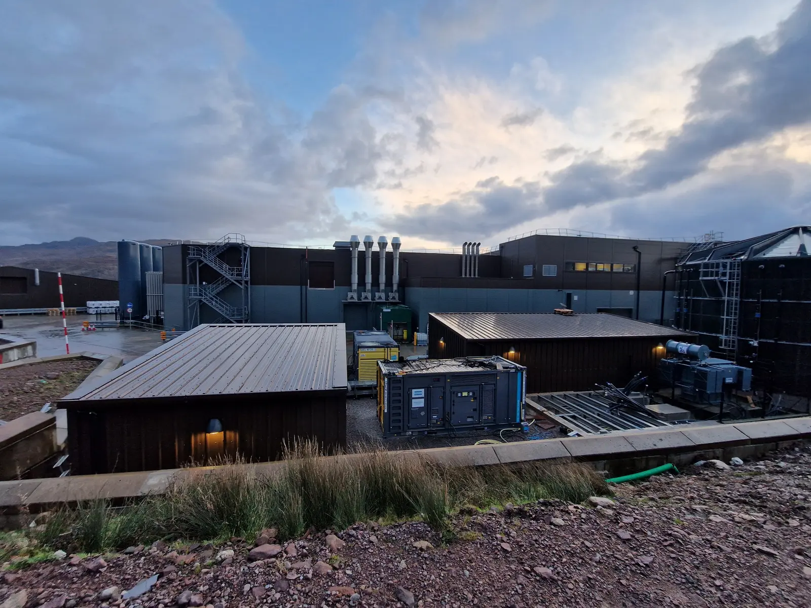 Four generator exhaust stacks above a plant building at dusk, Applecross